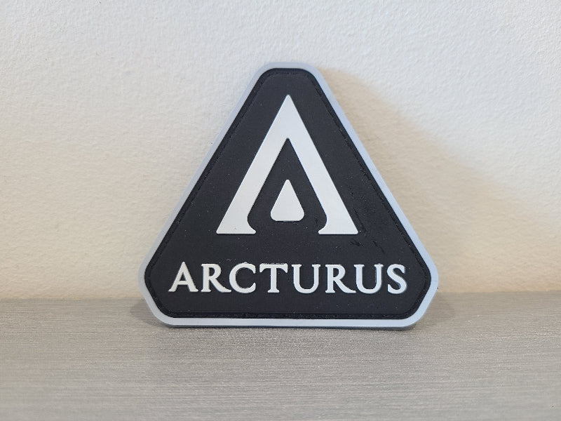 Arcturus PVC patch black triangle with white stylized A logo and ARCTURUS lettering on gray surface
